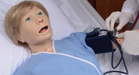 Profissional aferindo pressão arterial do simulador Susie em leito hospitalar